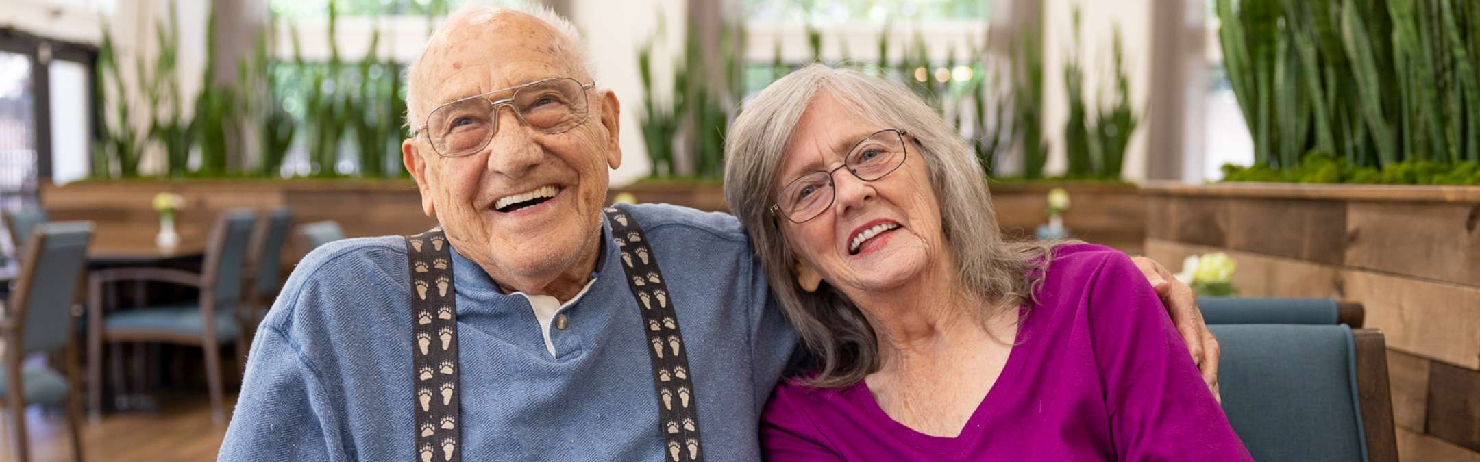 A cheerful elderly couple smiles while seated together in a bright, cozy space at Carlton Senior Living.