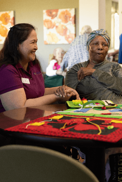 A Carlton Senior Living team member smiling while assisting a senior resident during an activity, representing the Positive Approach to Care.