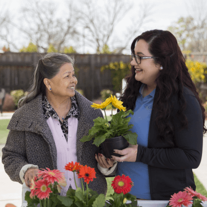 A Carlton Senior Living staff member holding a potted plant, sharing a smile with a senior resident during a gardening activity.