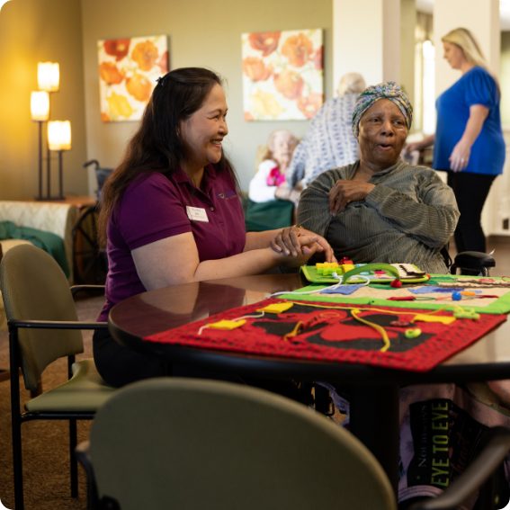 A senior resident and a Carlton Senior Living staff member smiling while working on an activity at a table, representing a supportive and engaging environment.